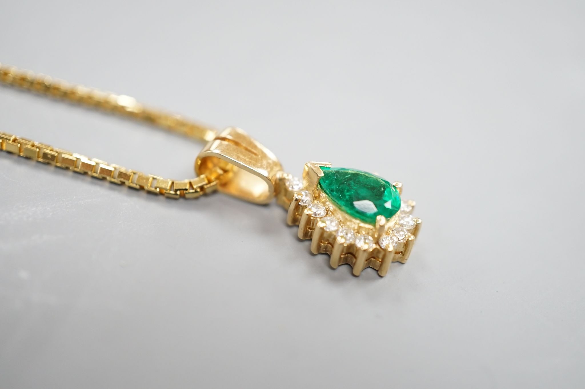A modern 18k, emerald and diamond cluster set pear shaped pendant, overall 21mm, on an 18k chain, 43cm